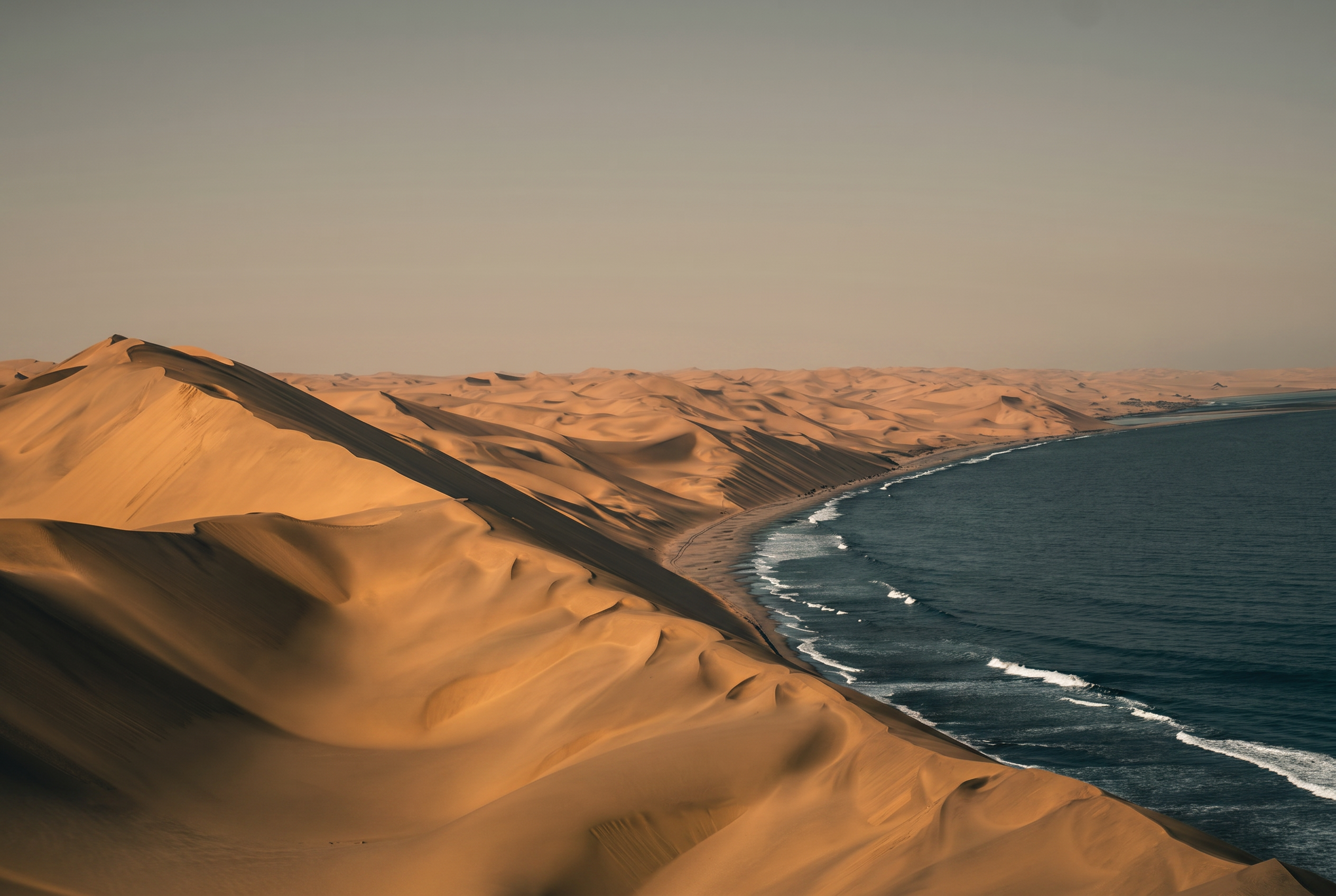 Golden desert dunes meeting a calm sea at dusk