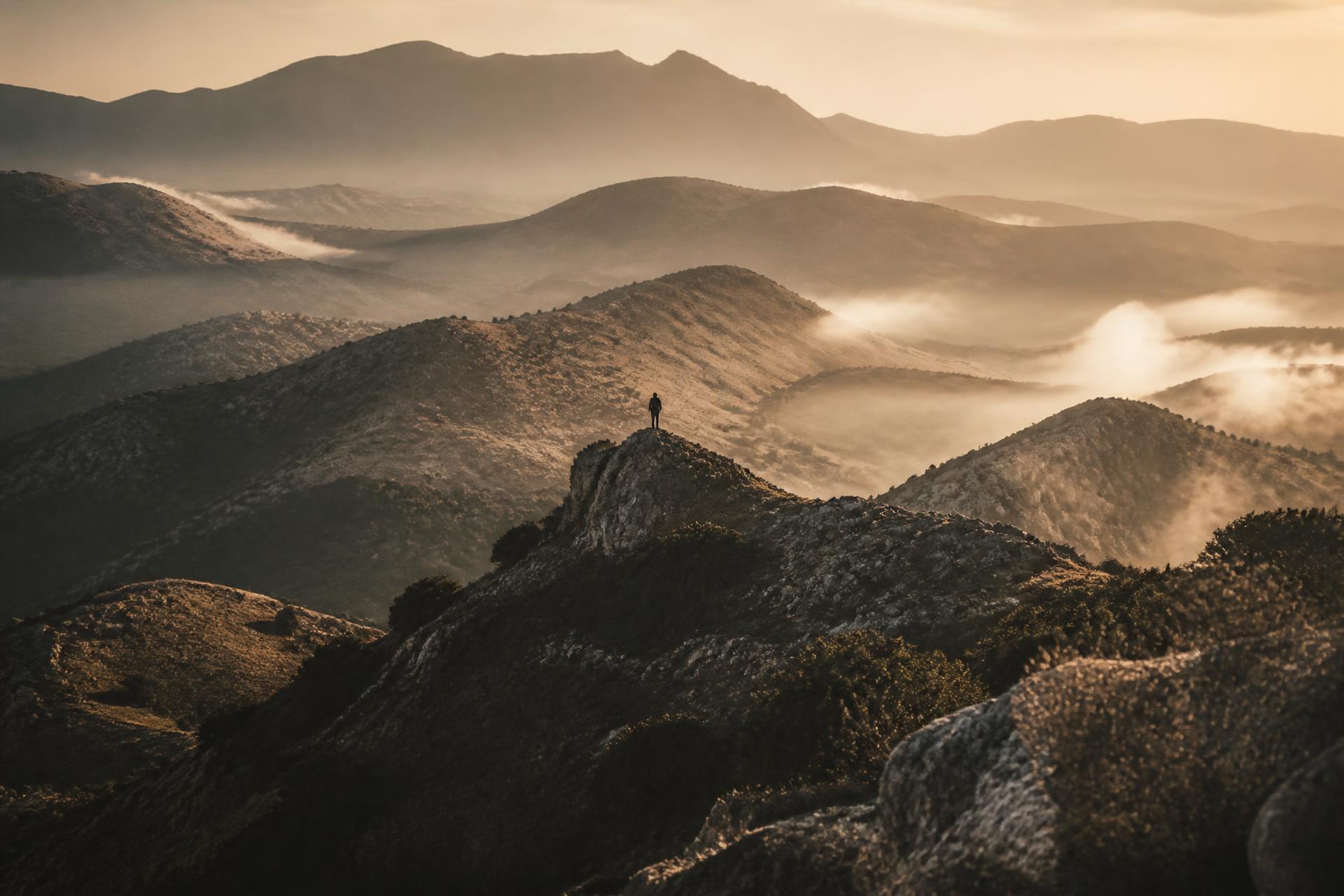 A lone figure standing on a mountain ridge at dawn above mist-filled valleys